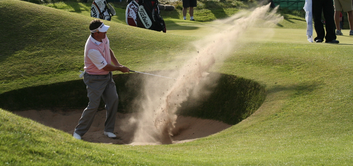 Lee Westwood in grey pants swinging Iron from the bunker